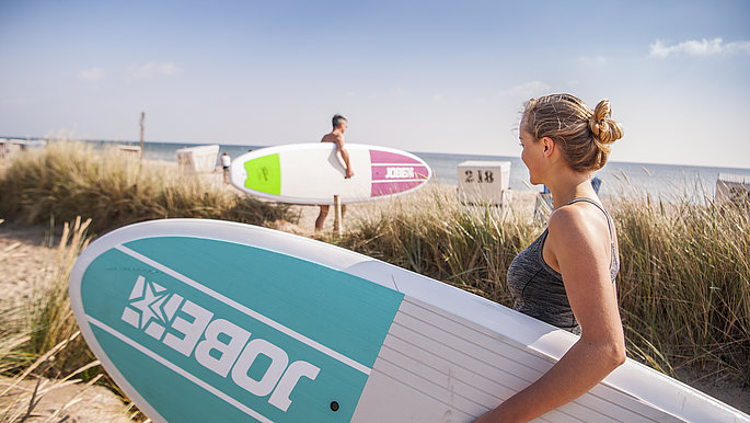 Eine Frau mit einem SUP Board unter dem Arm geht zum Wasser am OStseestrand