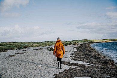 Ein Winterstrand auf Fehmarn, eine Frau mir orangefarbener JAcke steht mit dem Rücken zur Kamera im Wind