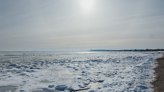 Schneelandschaft an der Ostsee Schleswig-Holstein mit schneebedecktem Strandsand und der glitzernden Sonne im Gegenlicht