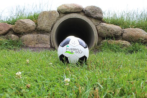 Ein Fußball liegt auf einer grünen Wiese vor einem Hindernis-Loch, das er überwinden muss auf der Fußballgolf Anlage am Weissenhäuser Strand an der Ostsee.